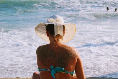 Rear view of mid adult woman sitting at beach