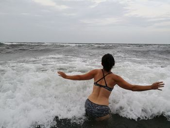 Rear view of woman standing in sea against cloudy sky