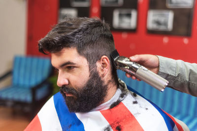 Cropped hand of barber cutting male customer hair in salon