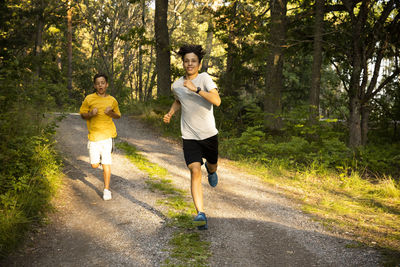 Excited boys running together on dirt road in forest during vacation