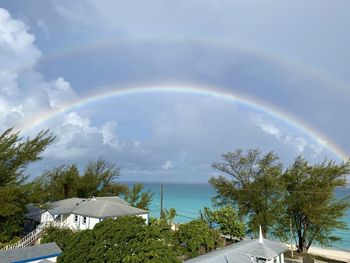 Rainbow over building and trees against sky