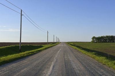 Empty road amidst field against clear sky