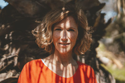 Smiling blond woman standing in front of tree