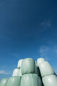 Low angle view of covered hay bales against blue sky on sunny day