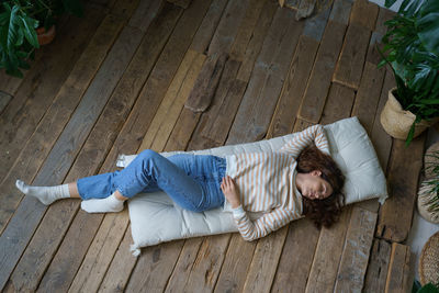 Calm woman lying on wooden floor surrounded by houseplants, rest in home garden. wellness concept