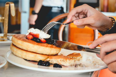 Cropped image of hands holding fork and table knife over pancakes