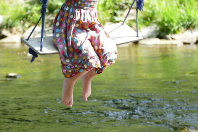 Low section of girl swinging over lake