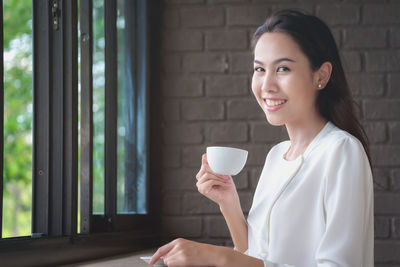 Portrait of smiling young woman holding coffee cup at home