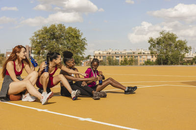 Happy friends having fun sitting in sports court on sunny day