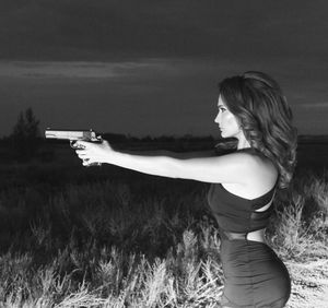 Side view of woman using handgun on field