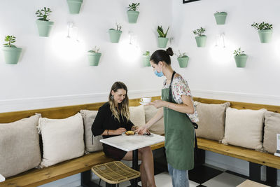 Barista wearing face mask serving food and dink to businesswoman while standing at coffee shop