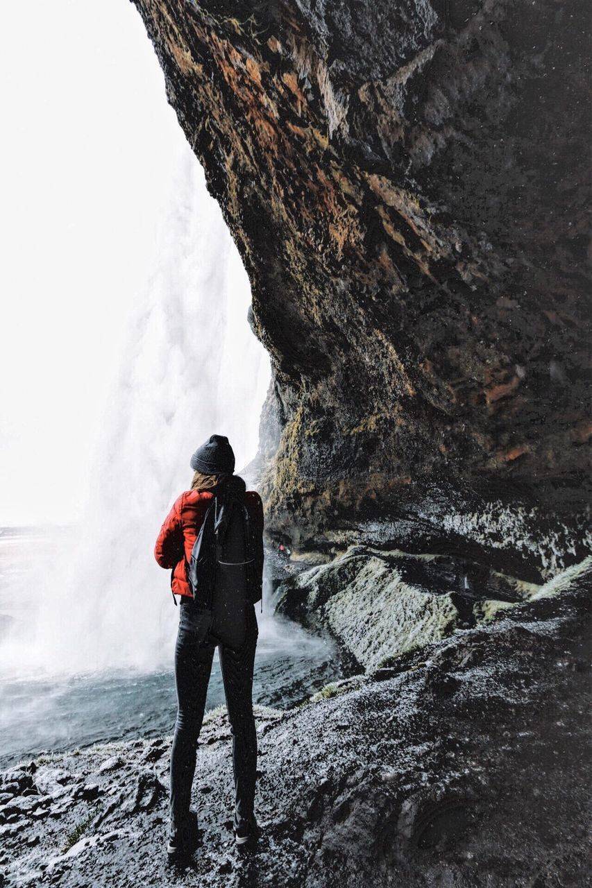 FULL LENGTH REAR VIEW OF MAN STANDING ON ROCK AGAINST SKY