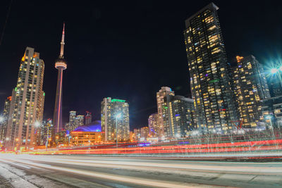 Light trails on road by illuminated buildings in city at night