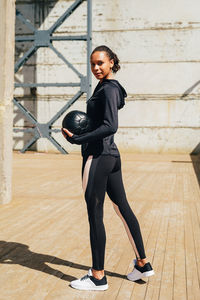 Full length of woman exercising with ball on boardwalk during sunny day