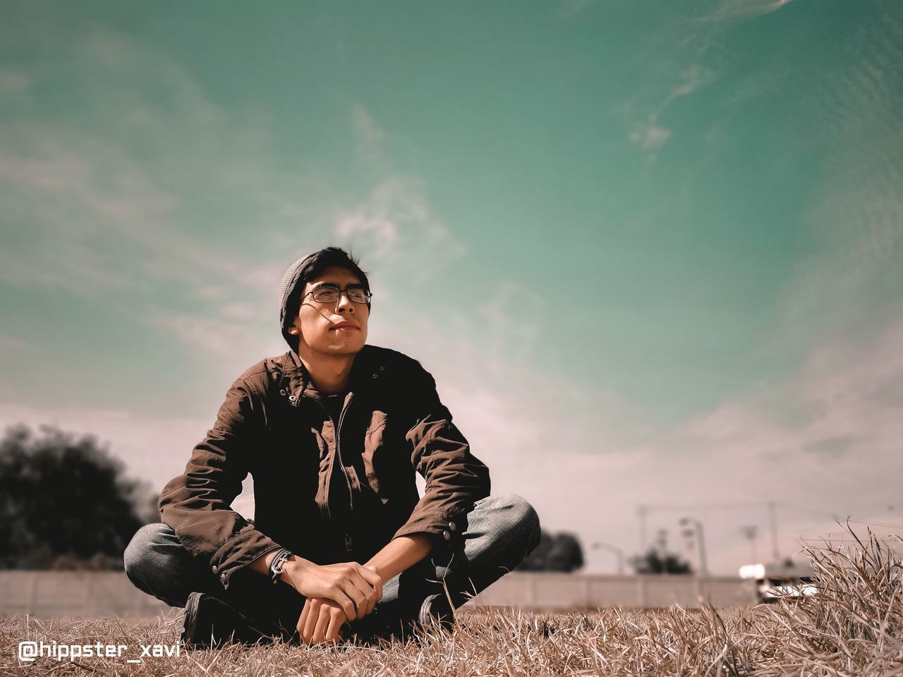 YOUNG MAN SITTING ON FIELD AGAINST SKY