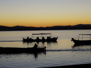 Silhouette people in boat on lake against sky during sunset