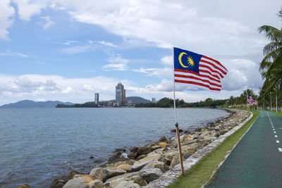 Malaysian flags on road by river against cloudy sky