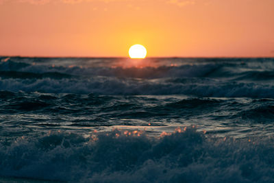 Half sun below horizon over blue sea waves, beautiful sunset overseas. turquoise sea in sunshine