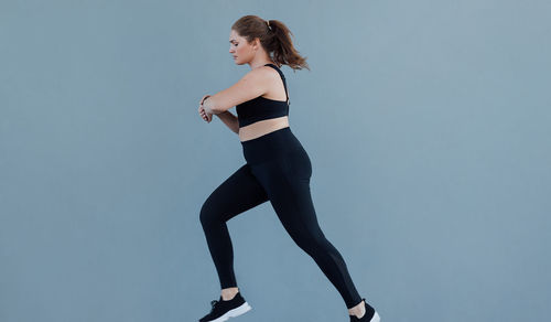 Full length of woman exercising against blue background