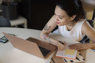 Woman with paraplegia writing in diary while looking at laptop