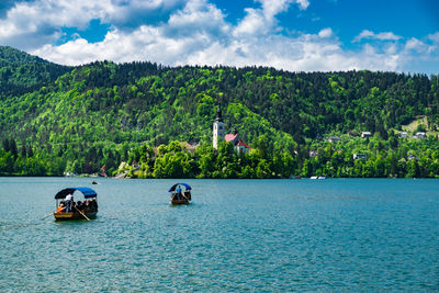 Boats on lake bled against tree mountain