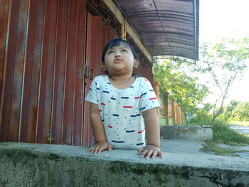 Cute girl looking away while standing against wall