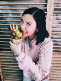 Portrait of beautiful woman holding fruit waffle against wall at home