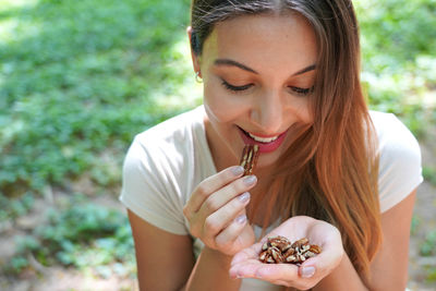 Close-up of healthy woman eating pecan nuts in the park. looks at nuts.