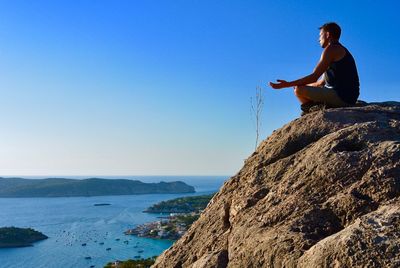 Side view of young man on cliff by sea against clear sky