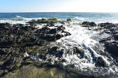 Splashing pacific ocean wave spraying against rocky coastline of calm tidal pools in baja, mexico