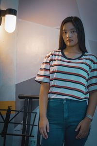 Portrait of young woman standing against wall at home