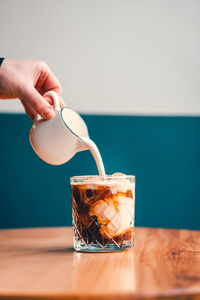 Person pouring cream into iced coffee 