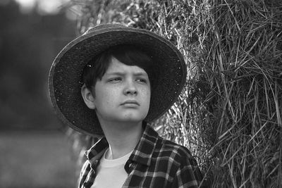 Black and white portrait boy in straw hat standing near hay bale in a field.