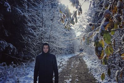 Portrait of man standing on dirt road amidst snow covered trees