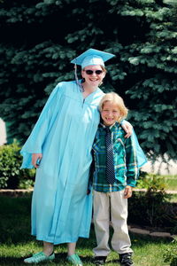 Full length portrait of smiling graduate with brother on field
