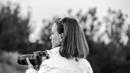 Rear view of woman with dslr against trees