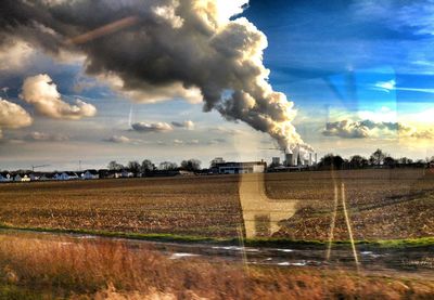 Smoke emitting from chimney on field against sky