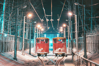 Trains on snow covered railroad tracks amidst illuminated street lights at night