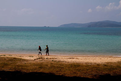 Man and woman walking on beach against sea