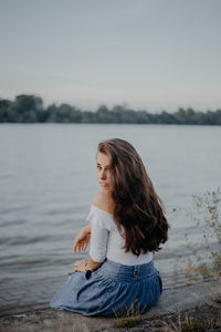 Portrait of woman sitting by lake against sky