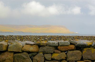 Stone wall by sea against sky