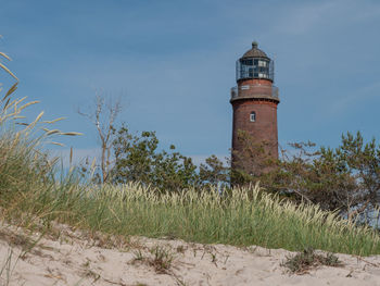 Lighthouse on field by building against sky