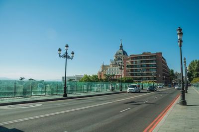 Almudena cathedral dome behind buildings on street with light posts in madrid, spain.