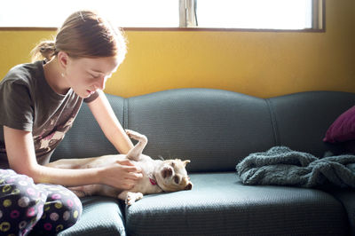 Girl playing with dog while sitting on sofa
