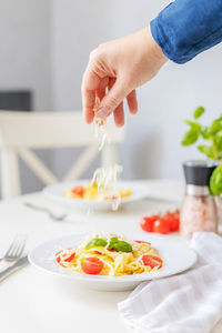 Girl's hands adding, sprinkles grated cheese to italian homemade pasta with cherry tomatoes. serving 