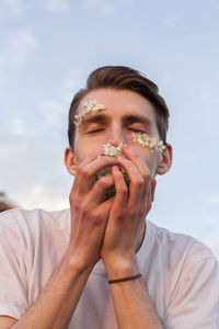 Close-up of man smelling flower against sky