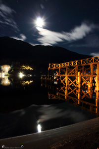 Illuminated built structure by sea against sky at night