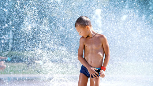 Excited boy of seven years having fun between water jets, in fountain, run around, sprinkle, have