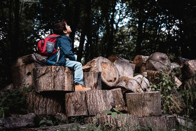 Boy sitting on logs against trees