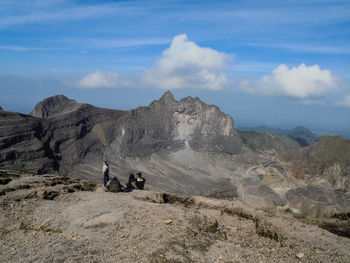 Friends sitting on landscape while looking at mountains